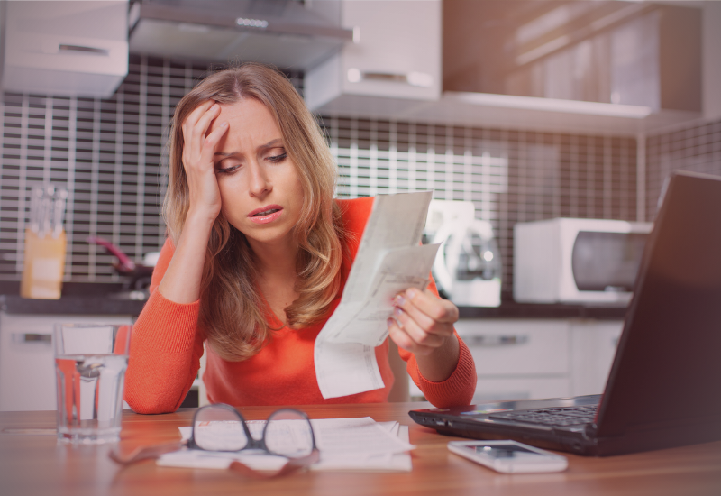 Mulher pensativa olhando contas e boletos sobre a mesa, refletindo sobre dívidas e inteligência financeira.