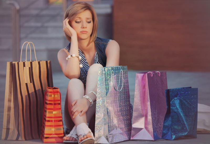 Mulher com sacolas de compras com expressão de arrependimento e tristeza.