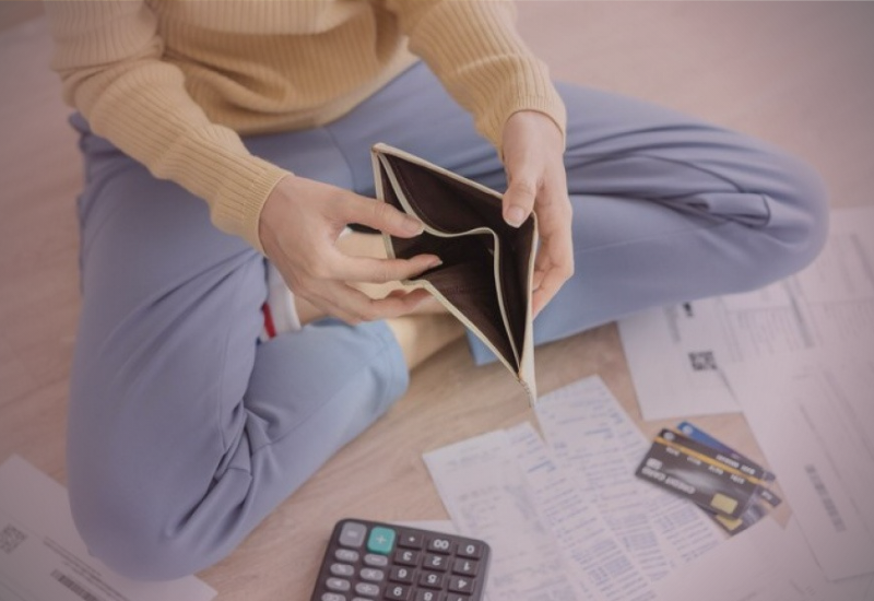 Mulher segurando carteira vazia e tendo contas e boletos para pagar.