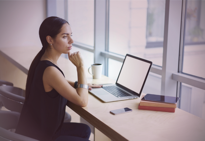 Mulher empreendedora refletindo enquanto trabalha no notebook em ambiente organizado, representando construção de negócio mesmo diante de desafios emocionais