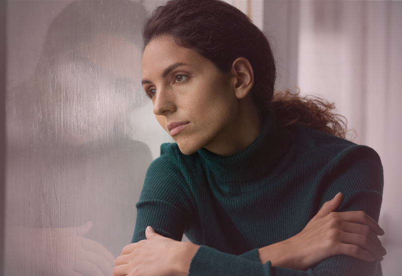 Mulher sentada em silêncio, com expressão reflexiva, em um ambiente interno neutro, representando o impacto emocional da negação e da invalidação de experiências vividas.