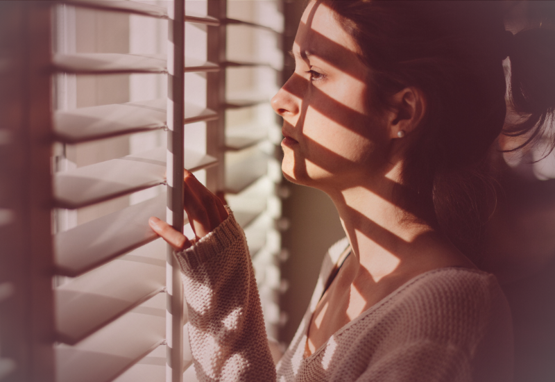 Mulher em pé próxima a uma janela, olhando para fora com expressão reflexiva, simbolizando consciência emocional, limites saudáveis e responsabilidade individual.