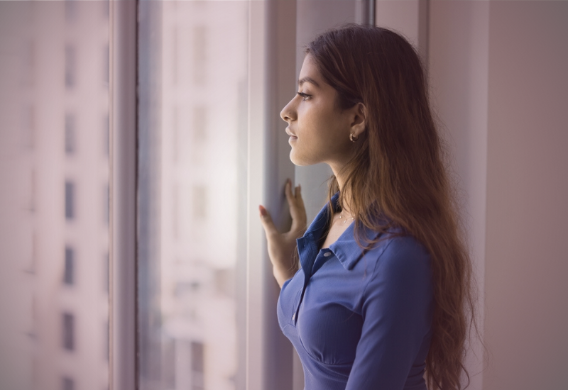 Mulher em pé olhando pela janela, refletindo com postura firme sobre apoio emocional, maturidade e responsabilidade nos relacionamentos.