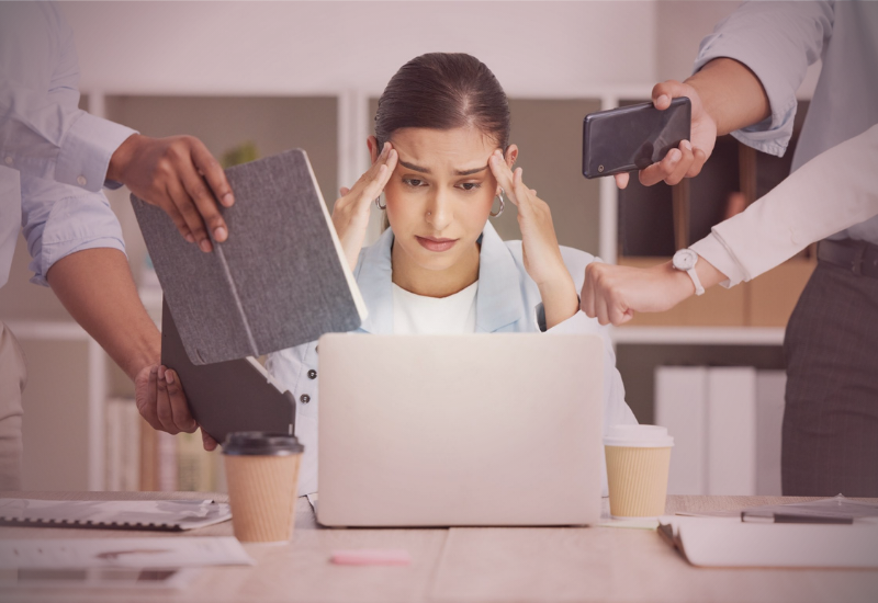 Mulher sobrecarregada recebendo múltiplas demandas ao mesmo tempo enquanto trabalha no computador.